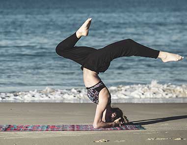 Женщина занимается йогой на берегу пляжа.
